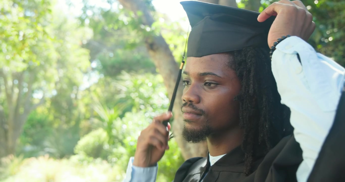 African American man checking fit adjusting cap fixing gown checking tassel in park, copy space