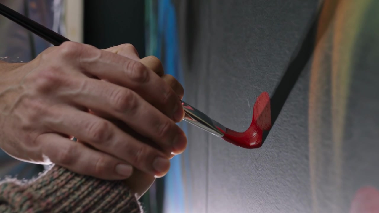 Un tutor posa la mano sulla mano di un allievo, guidando un pennello con la punta rossa su un pannello, durante una lezione.