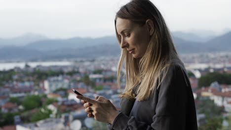 woman using a smartphone while standing on top view point of the city