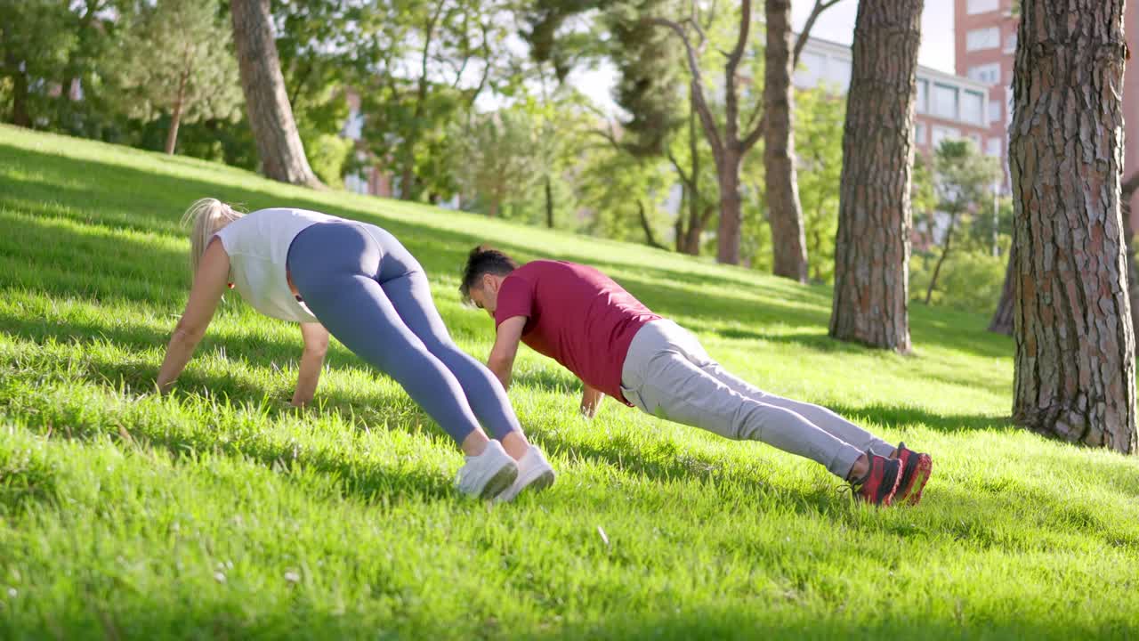 Man and Woman Doing Push Ups on Grassy Hill in Park