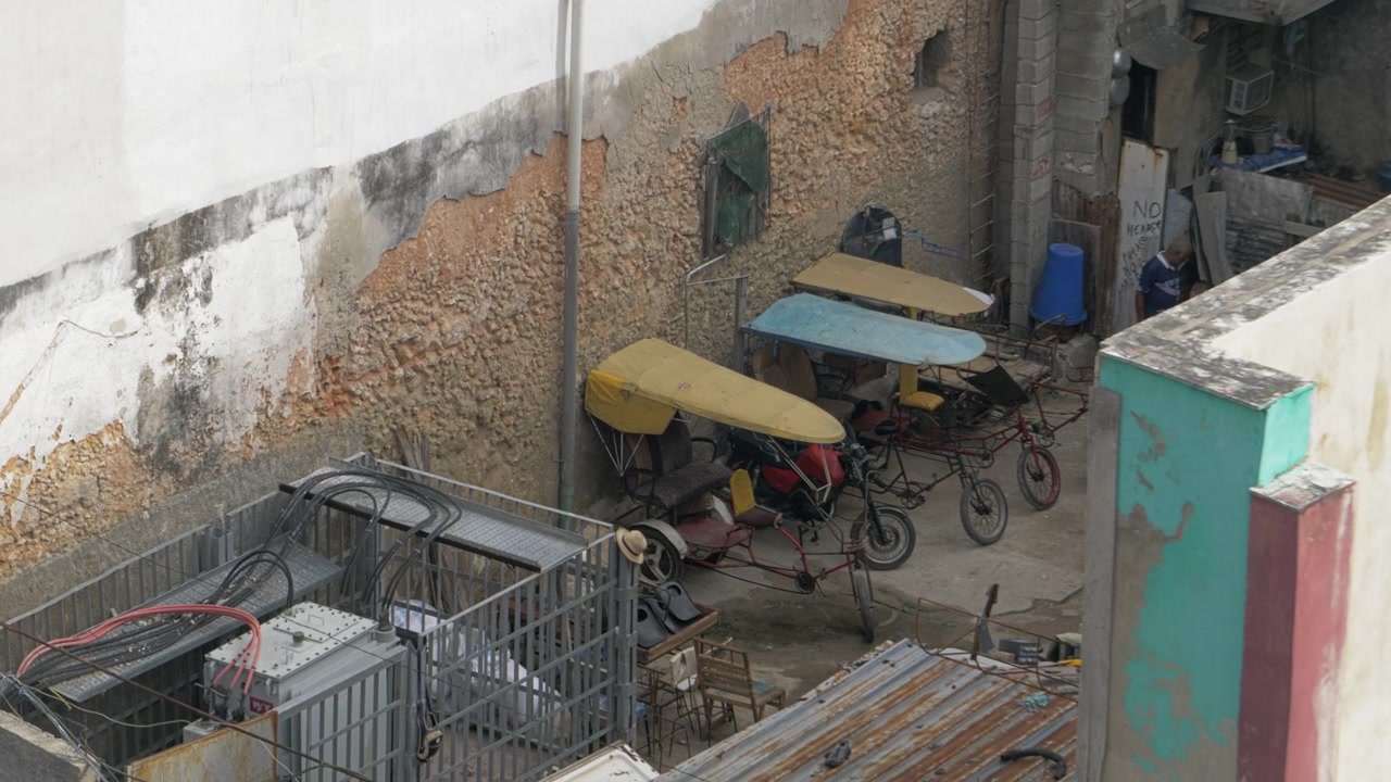 Vista aérea de un patio en La Habana, Cuba, con bicitaxis estacionados, toldos de colores, paredes desgastadas, bicicletas y estructuras de servicios públicos para temas de transporte local al aire libre