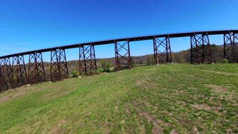 A-low-angle-aerial-view-with-an-FPV-drone-flying-under-the-Moodna-Viaduct-in-Salisbury-Mills,-NY-on-a-sunny-day