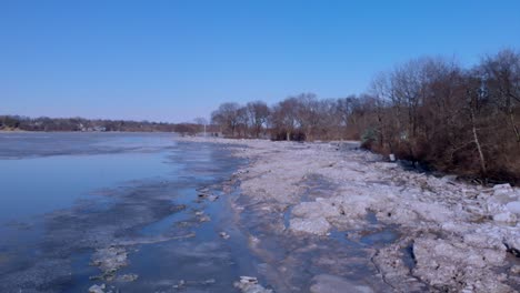 Langsamer-Drohnenschuss,-Der-über-Einen-Teilweise-Zugefrorenen-Fluss-Entlang-Des-Bewaldeten-Flussufers-Fliegt