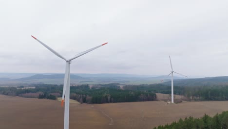 Drone-shot-of-windmills-rotating-during-daytime-with-beautiful-landscape-at-background