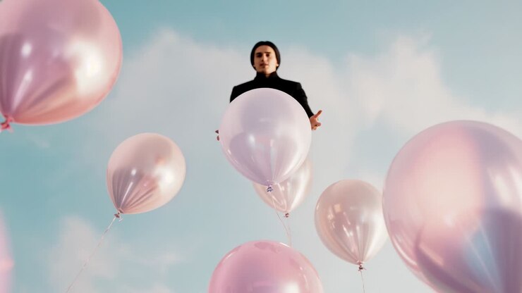 Palloncini metallici in aumento che sollevano un uomo con una giacca scura in vista, che apre le braccia in segno di benvenuto sullo sfondo del cielo