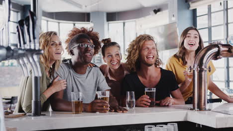 group of male and female friends celebrating whilst watching game on screen in sports bar