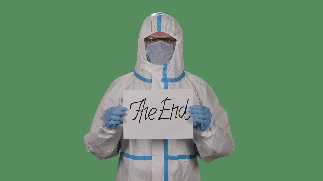 보호복, 보호 안경, 장갑 및 호흡기를 입은 남자의 초상화, 끝 표지판을 들고 카메라를 바라보고, 녹색 스크린, 크로마 키, 코로나 바이러스 사망 개념, 느린 모션, 클로즈업