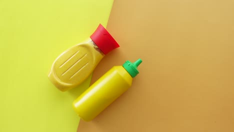 dos botellas de mostaza sobre un fondo amarillo y naranja
