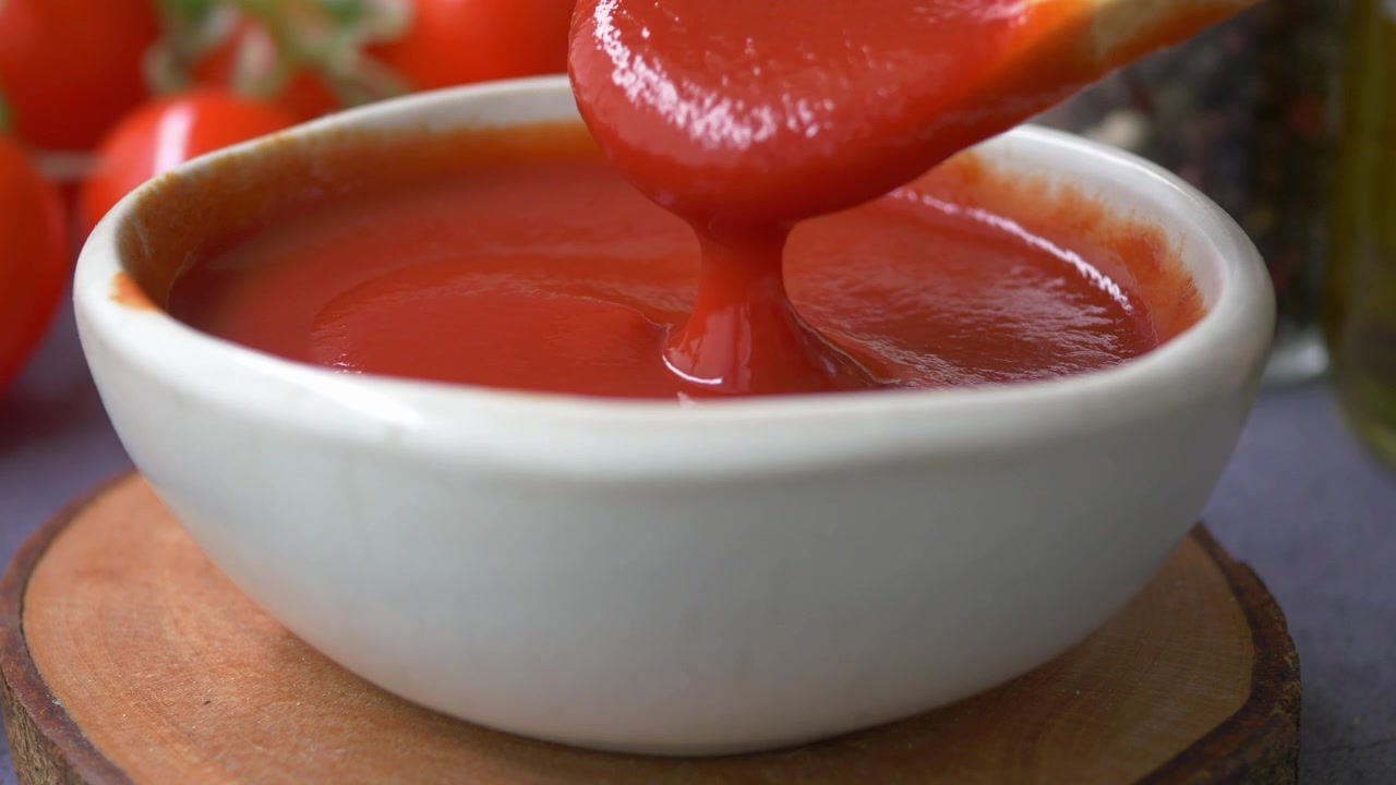 Holzlöffel rührt frische Tomatensoße in einer weißen Schüssel