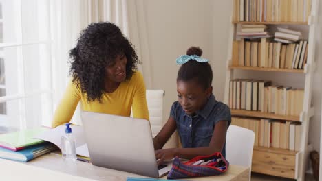 African american mother and daughter smiling while looking at each other and using laptop