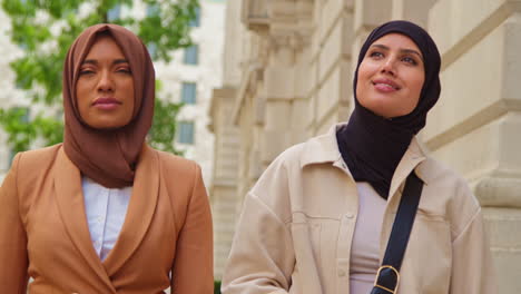 two muslim businesswomen wearing hijabs with modern business suits walking to work past city office buildings 3