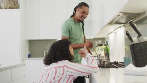 Happy-biracial-woman-in-wheelchair-talking-with-smiling-male-partner-preparing-food-in-kitchen