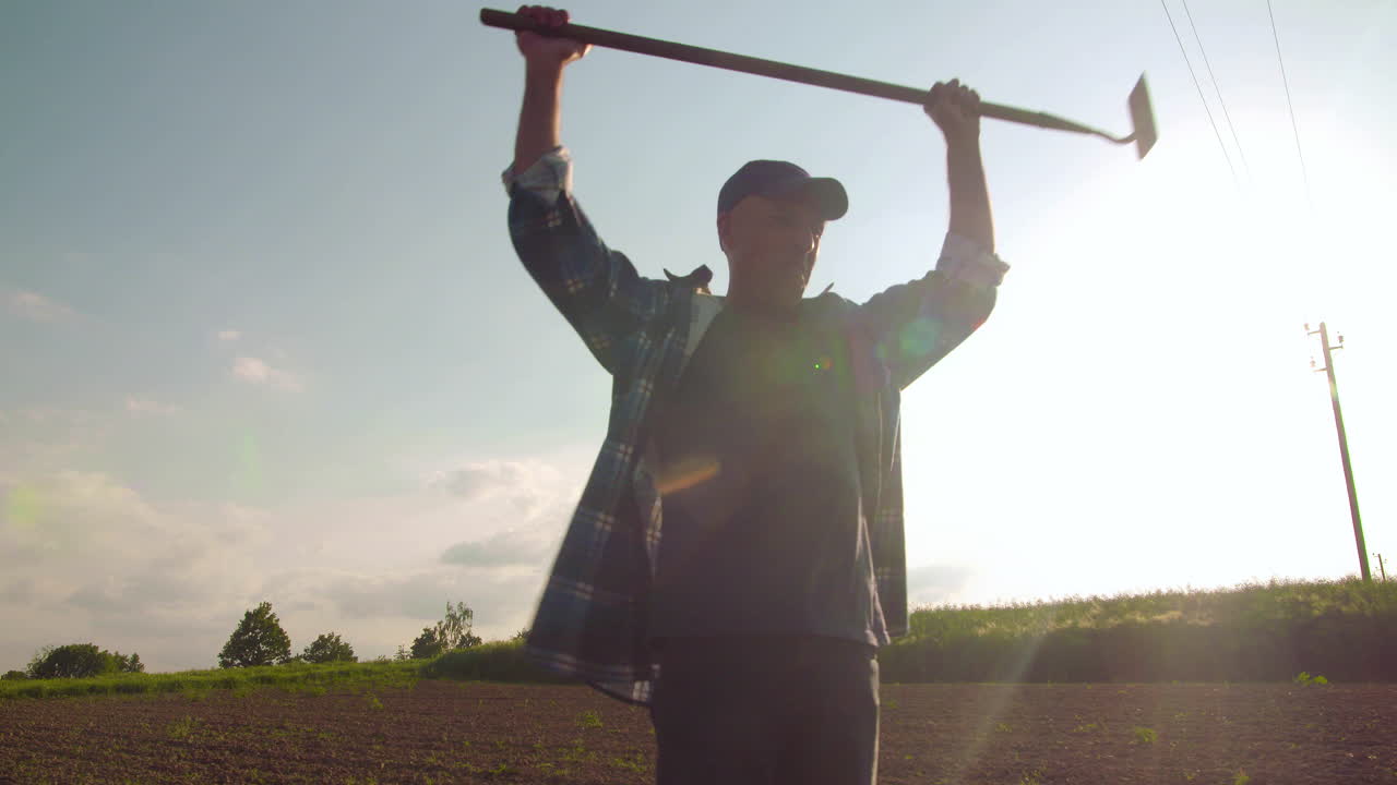 Hombre balancea azada en un campo agrícola soleado.