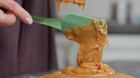 close-up of thick, creamy brown batter falling from green spatula onto flour on countertop, smooth texture and rich consistency highlight homemade baking process