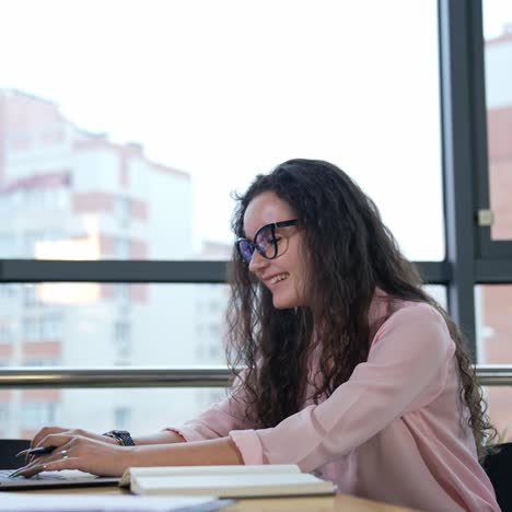 beautiful woman working at computer and smiling. female worker in a good mood works in an office. workplace in big light office with large windows