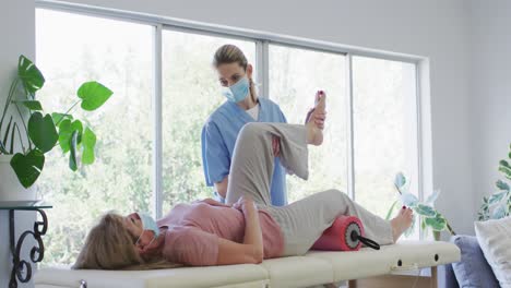 Female-health-worker-stretching-leg-of-senior-woman-at-home