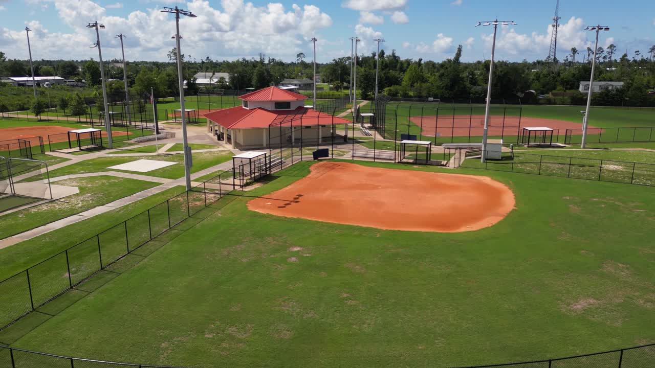 Pushing Drone shot from the edge of a scrapyard towards a small sports park with baseball fields and concession building