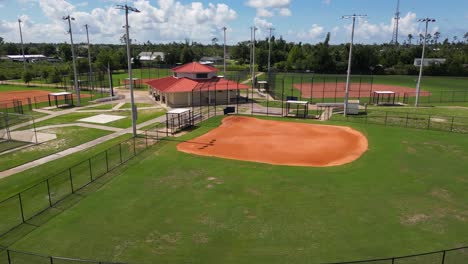 pushing drone shot from the edge of a scrapyard towards a small sports park with baseball fields and concession building