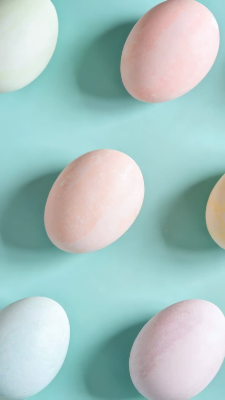 Vertical video: Camera panning downward, revealing pastel eggs on teal backdrop for product styling