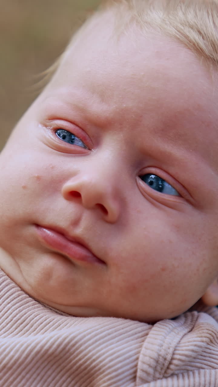 Blue-eyed blond infant boy looking really serious. Little baby just going to cry. Close up. Vertical video