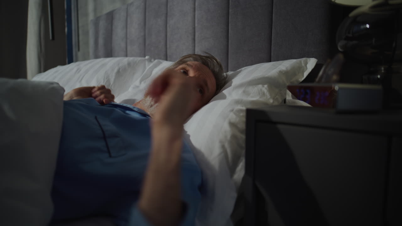 Middle Aged Man Wakes Up Early in Morning in Bedroom Filled With Sunlight