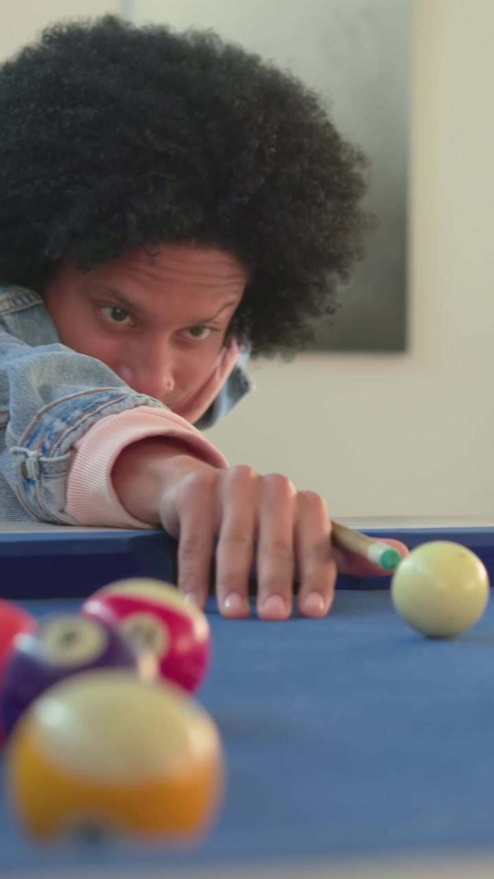 Vertical video: Leaning forward man lining up striking cue to sink ball at home blue table denim