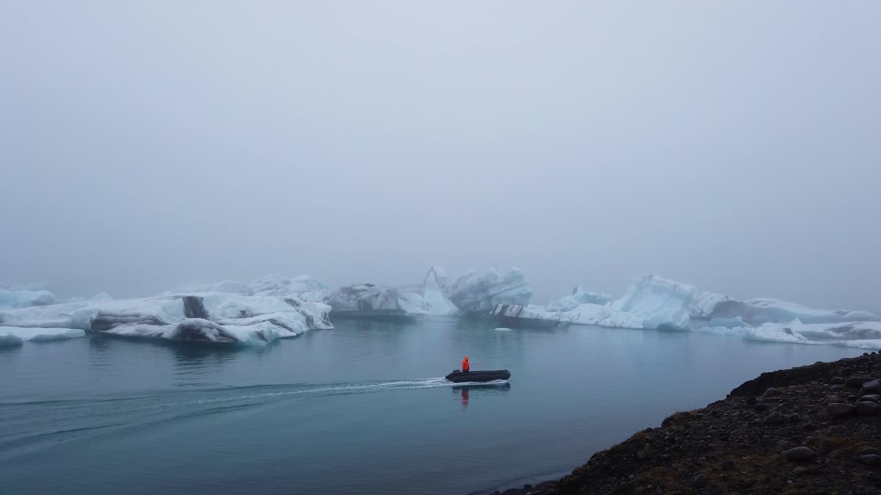 jokusarlon 빙하 석호에 떠있는 큰 빙산에 접근하는 조디악 보트에 밝은 주황색 재킷을 입은 사람