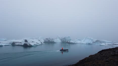 Persona-Con-Una-Chaqueta-Naranja-Brillante-En-Un-Bote-Zodiac-Acercándose-A-Grandes-Icebergs-Flotando-En-La-Laguna-Del-Glaciar-Jokusarlon