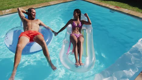 Diverse-group-of-friends-having-fun-playing-on-inflatables-in-swimming-pool