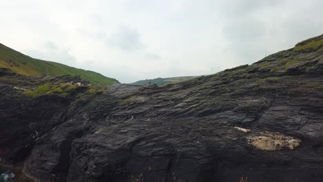 Hiker-standing-on-top-of-Cornwall-coastal-cliffs,-England,-aerial-flyover