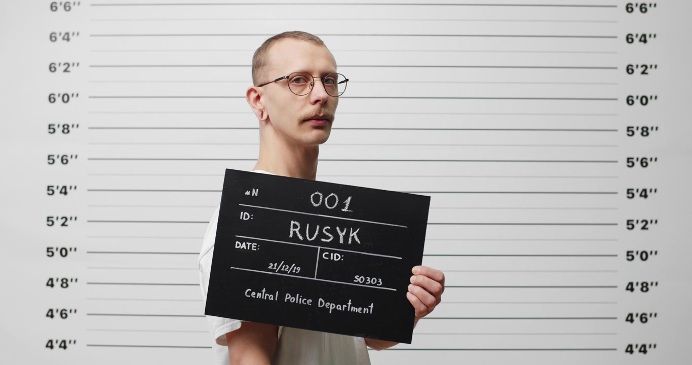 Mladý muž držící tabulku s identifikačními údaji na pozadí policejní identifikační řady