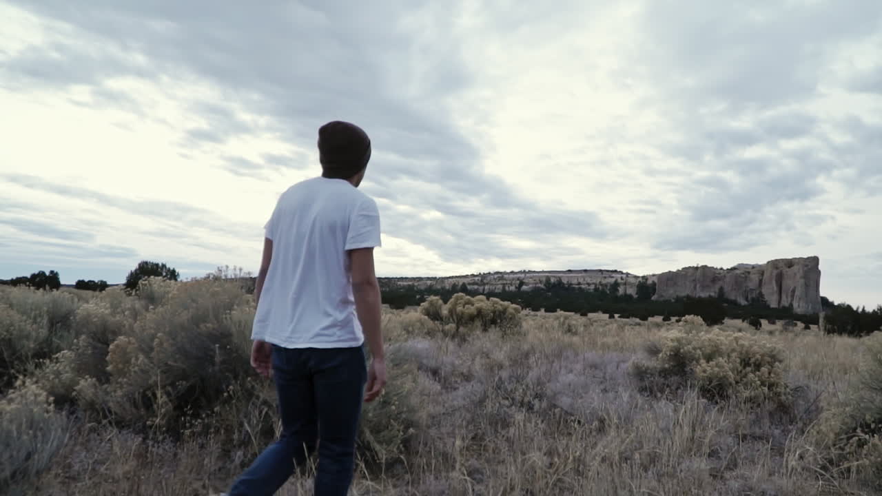 joven con gorro caminando por el paisaje del desierto, cámara lenta