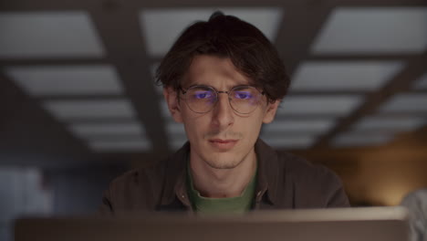 Concentrated Young Man Working on Laptop in Evening in Office
