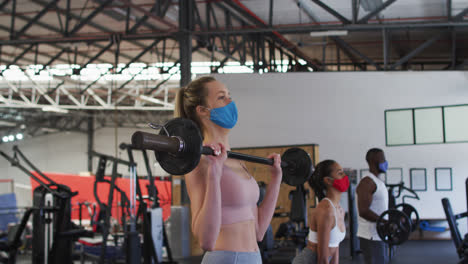 fit caucasian woman wearing face mask exercising using barbell in the gym