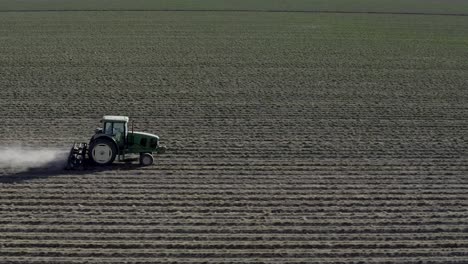 Tractor-ploughing-dry-farmland,-side-aerial-follow-view