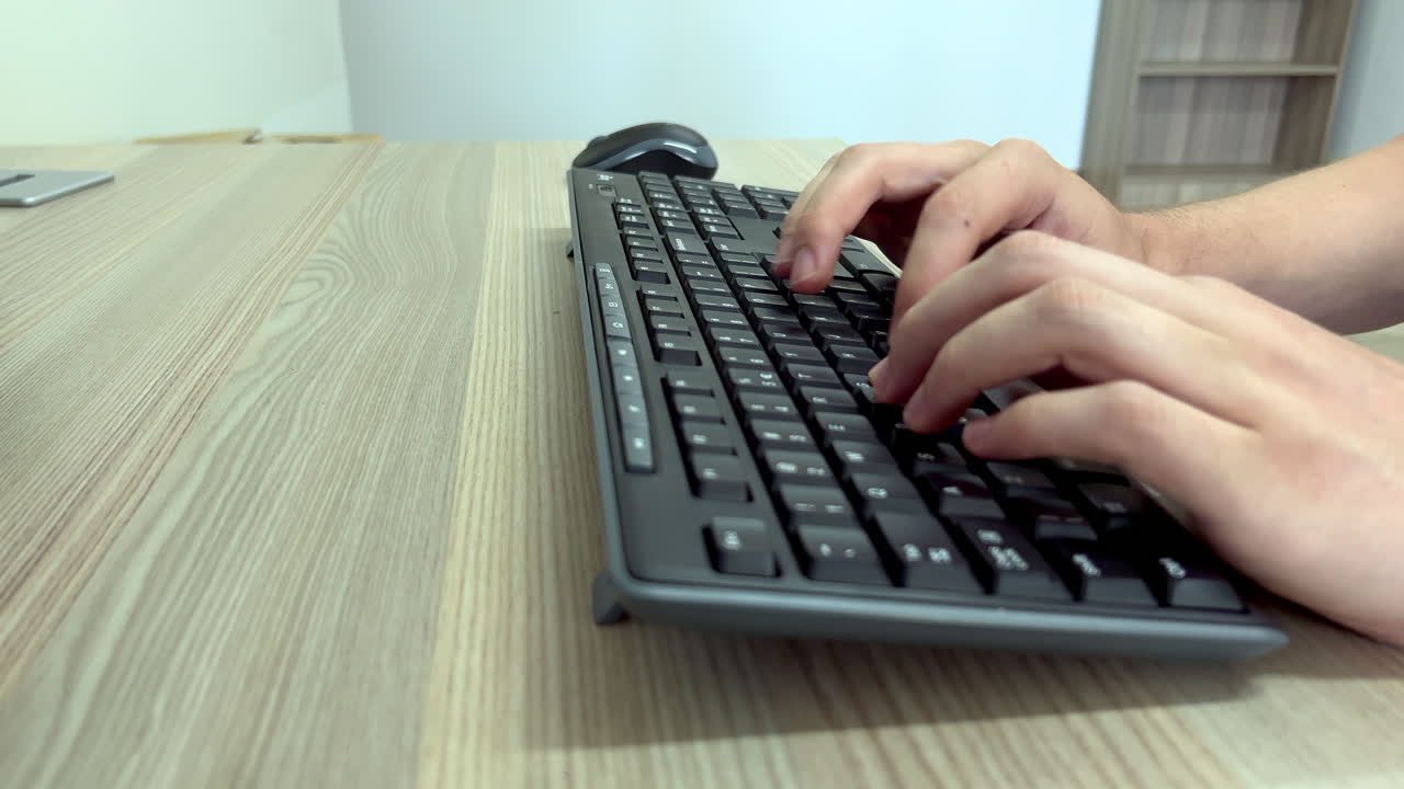 Closeup of hands typing on a computer keyboard on a wooden office desk