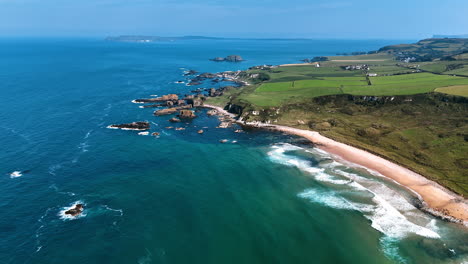 green rocky shore of ireland with rare houses scattered by the valley. footage above the waterscape of the atlantic ocean on sunny day.