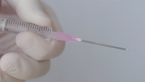 gotitas en jeringa hipodérmica mientras presiona con la mano en guante quirúrgico, primer plano