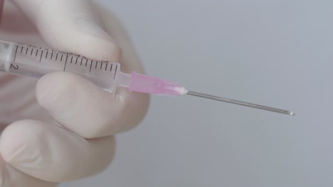 droplets on hypodermic syringe while pressing with hand in surgical glove, close up shot