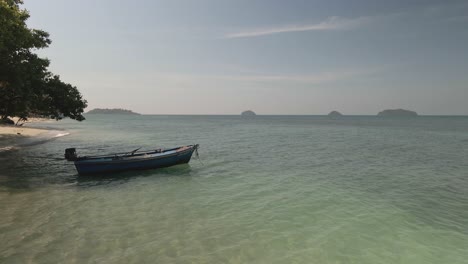 small-boat-moored-on-a-tropical-beach-with-islands-in-distance,-pan-right-shot