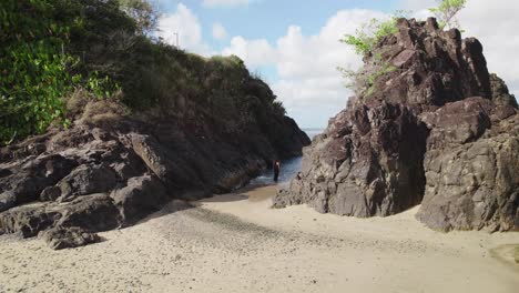 aerial view of a girl in a black dress walking into a ocean chanel with cliffs on both side