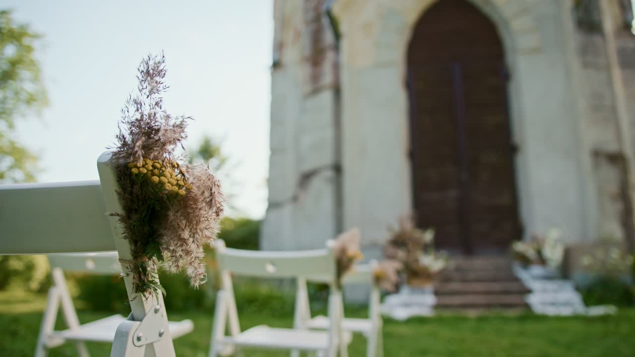 Wedding ceremony setup with decorated chairs and flowers near a chapel