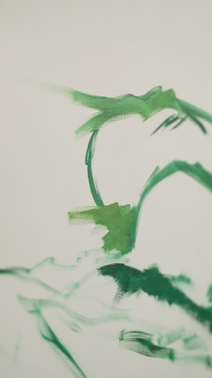 A close-up shot of a painter's hand as they create sweeping green brush strokes on a white canvas. The focus is on the hand's movement and the vivid green paint against the stark white background