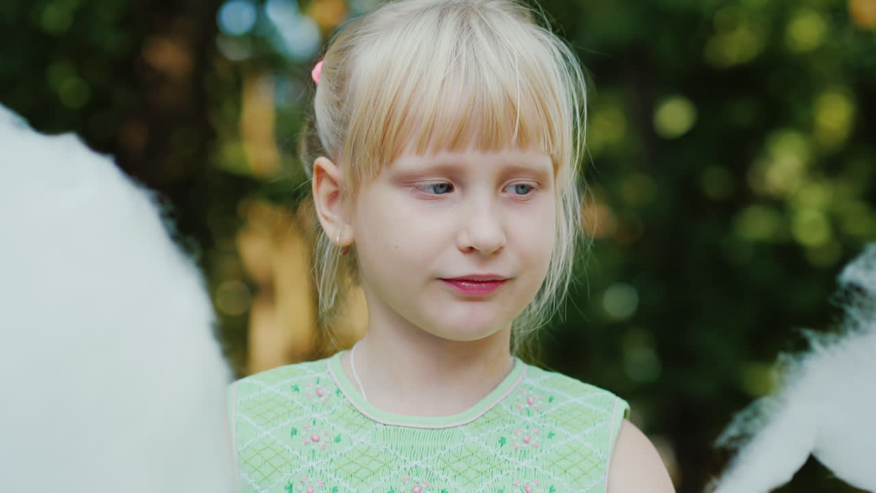 chica rubia fresca de 6 años está comiendo algodón dulce en el retrato del parque con poca profundidad de