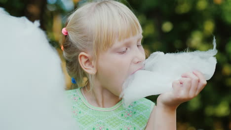 cool blonde girl 6 years old is eating sweet cotton wool in the park portrait with shallow depth of