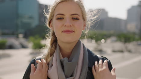 close up portrait of happy young blonde woman student smiling confident at camera running hands through hair in sunny urban city background