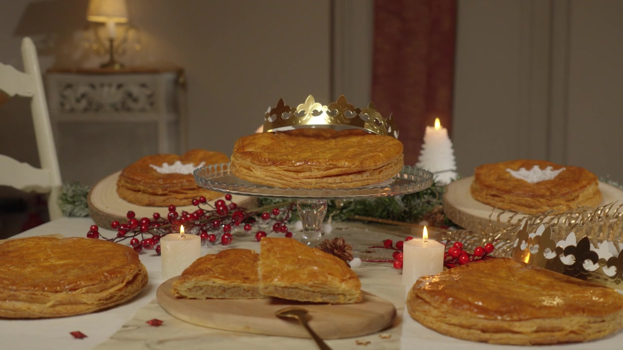 Şenlikli bir masada taçlar ve mumlarla sergilenen geleneksel galette des rois pastaları.