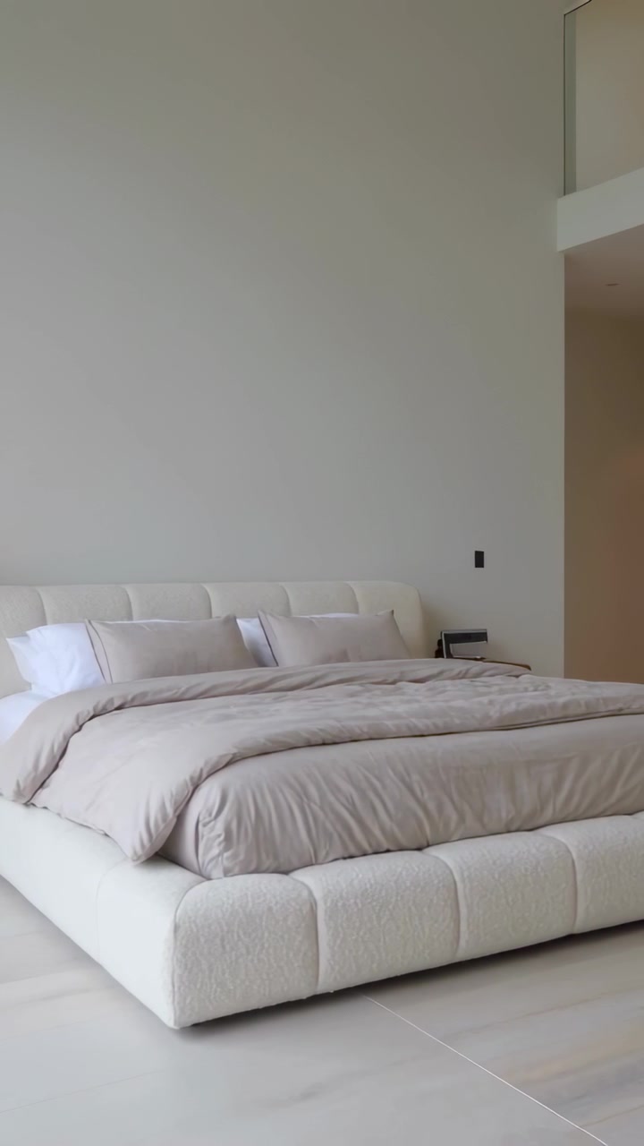 Video verticale: Inizio panoramica della telecamera su un letto basso con piumone color tortora e lampada da comodino per mostrare la disposizione.