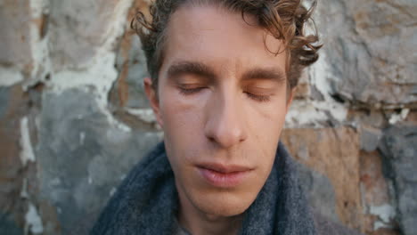 sad guy contemplating stoned wall closeup. elegant young man standing posing