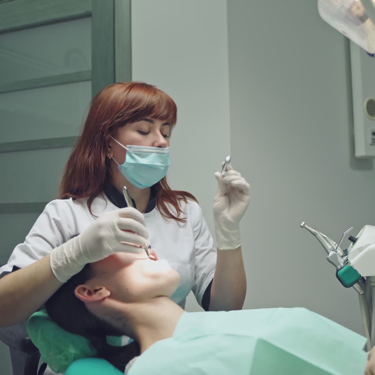 Beautiful dentist treating teeth to a woman patient in clinic over dental equipment background. Female professional doctor stomatologist at work.